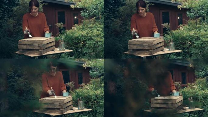 在花园里DIY。女人画木箱。