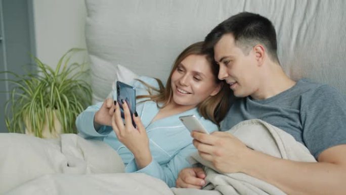 有魅力的男人和女人在床上使用智能手机在家里微笑