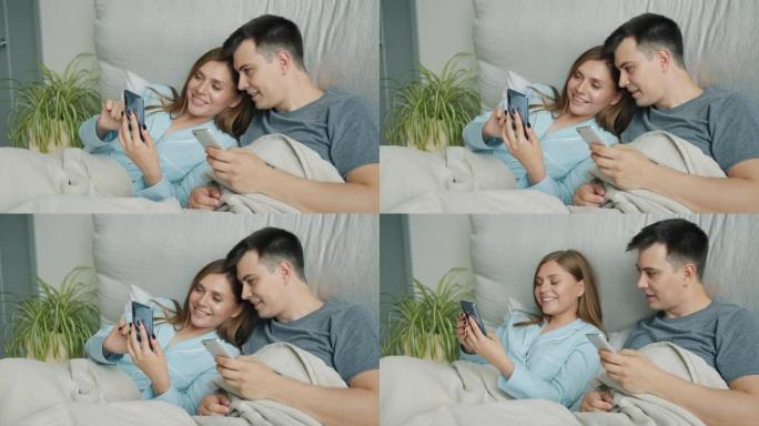有魅力的男人和女人在床上使用智能手机在家里微笑