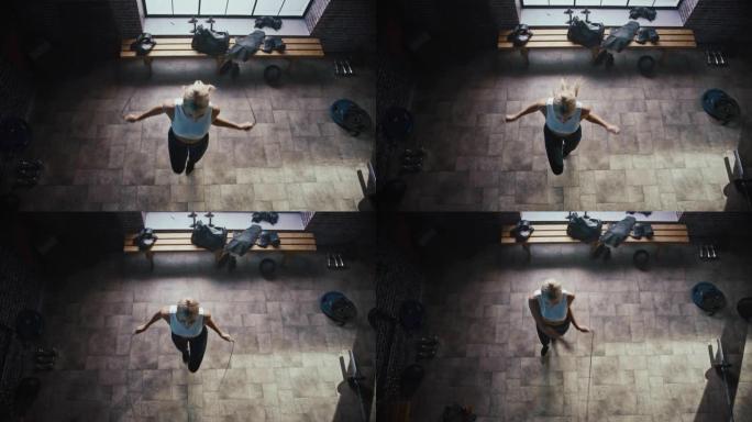 在硬核健身房穿着运动服和跳绳的运动美女。使用跳绳有氧运动进行健身训练。顶视图相机拍摄