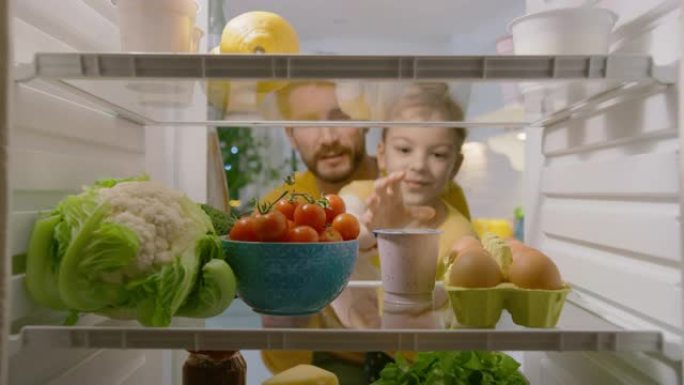 厨房冰箱内的摄像头: 爸爸打开冰箱门，抬起可爱的小女儿来选择她想要的任何东西，她选择健康的酸奶。从装