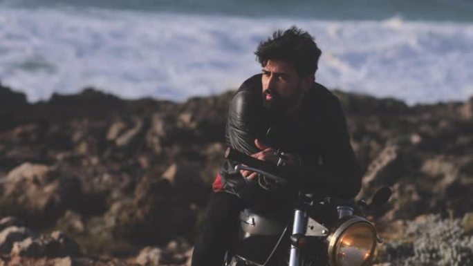 英俊的男人靠在海边的经典摩托车上