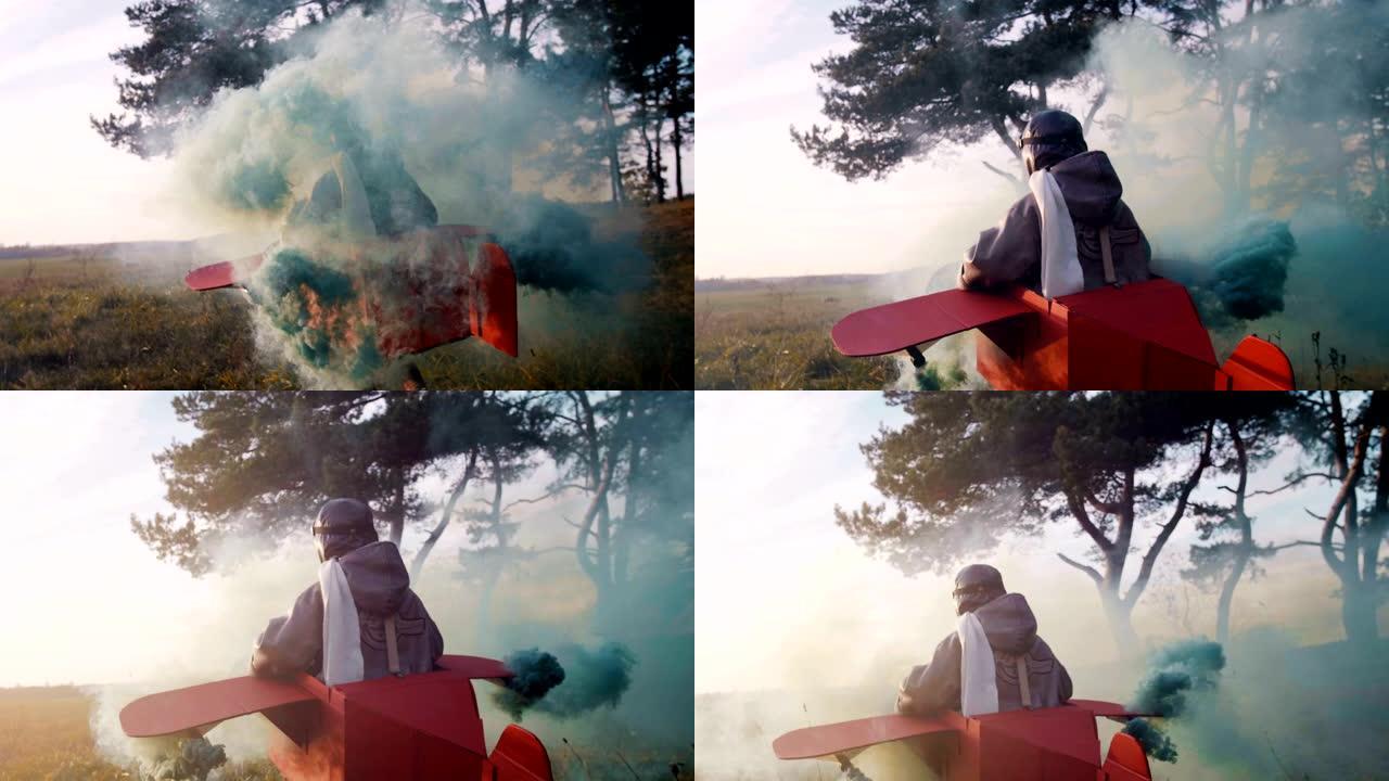 相机跟随快乐的小飞行员男孩穿着有趣的纸板飞机服装在户外奔跑，彩色烟雾慢动作。