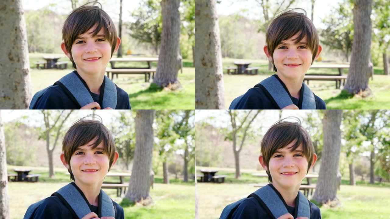 公园里背着背包的小男孩的慢动作肖像对着镜头微笑