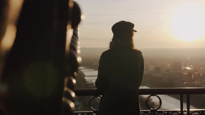电影滑梯镜头从埃菲尔铁塔的金属酒吧到快乐优雅的女子观看史诗般的巴黎日落天空的慢动作。