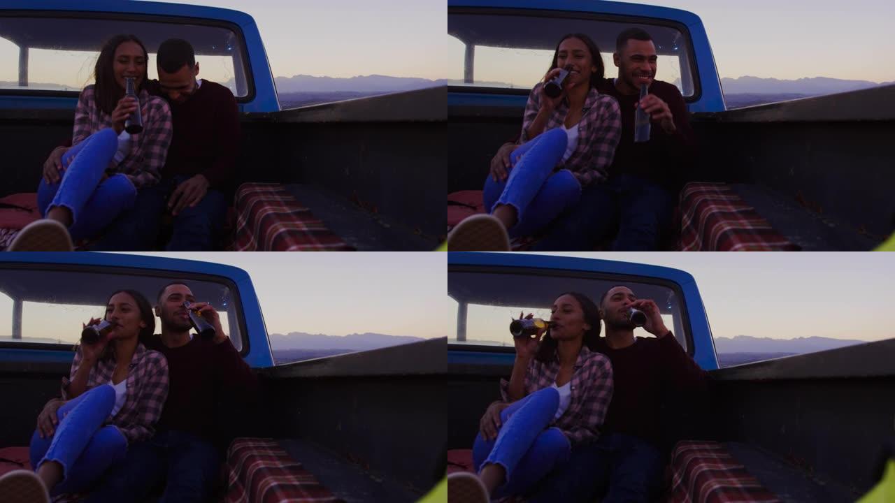 年轻夫妇在黄昏时坐在卡车外面的公路旅行中