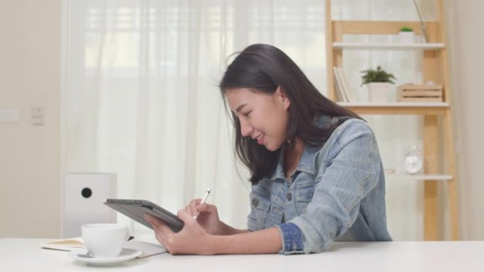 亚洲自由平面设计师女性休闲装在家里的客厅使用数字图形平板绘画。