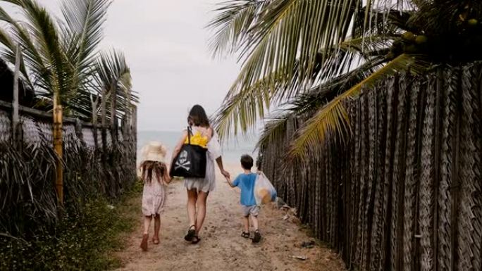 幸福的年轻家庭，母亲带着小儿子和女儿，一起走向美丽的海洋海滩度假。