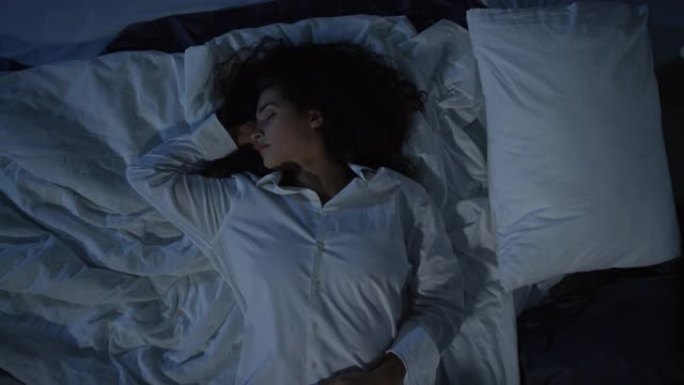 穿着男式衬衫的年轻女子在黑暗中睡在床上