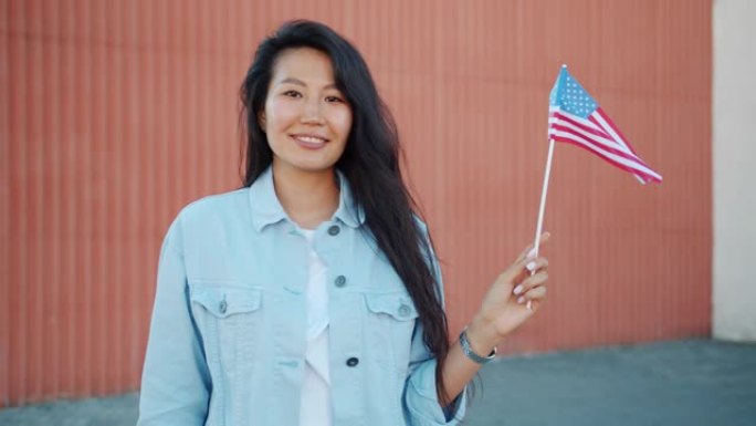 漂亮的亚洲女孩在户外举着美国国旗，微笑着看着相机的肖像