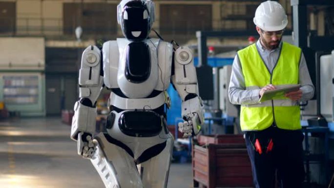 工厂工人使用平板电脑检查行走的机器人。