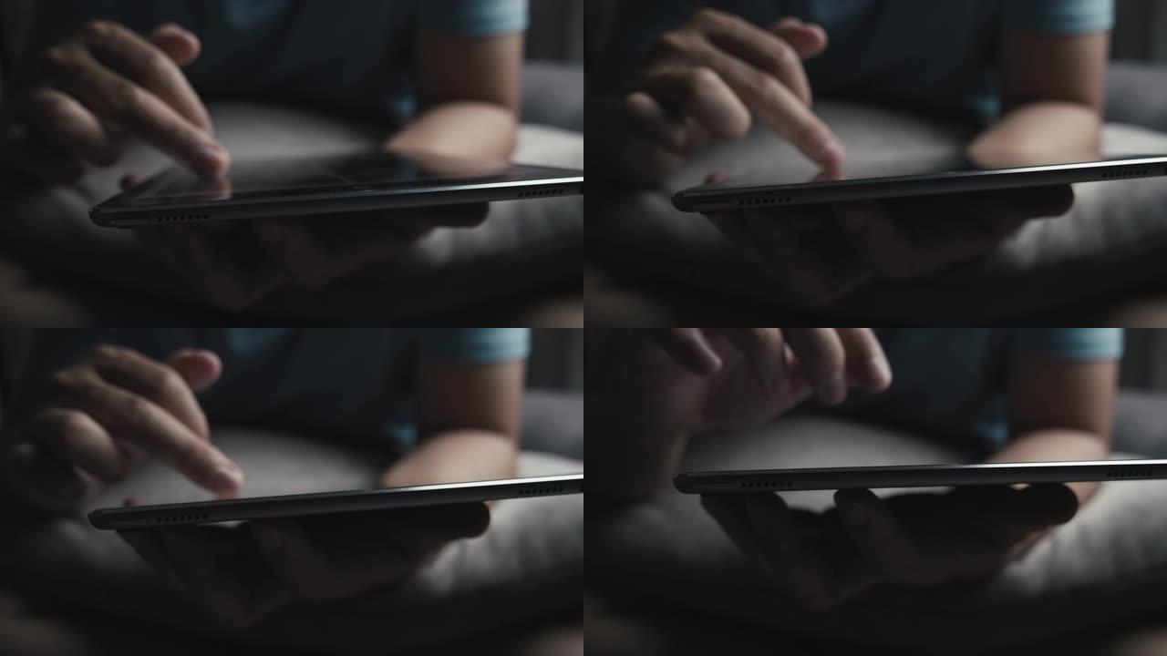 男人坐在灰色的沙发上，用平板电脑观看热气腾腾的在线内容。