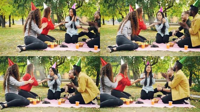 朋友们祝贺亚洲妇女生日给蛋糕带来惊喜，女孩在公园的户外聚会上吹蜡烛，微笑和拍手。