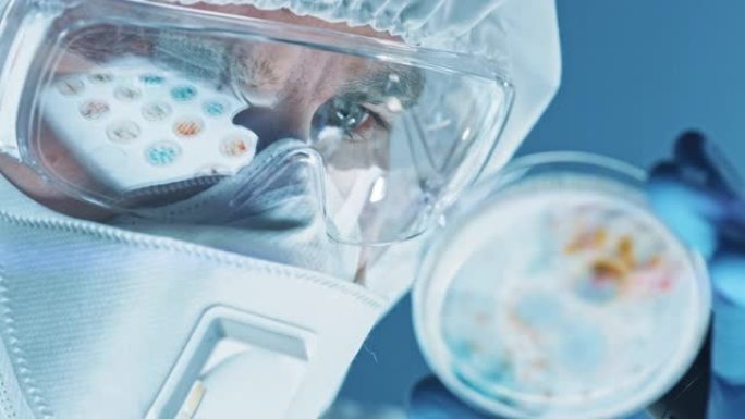 戴着呼吸器面罩，工作服和安全眼镜的科学家看着带有细菌，组织和血液样本的培养皿。治疗流行病的医学研究实