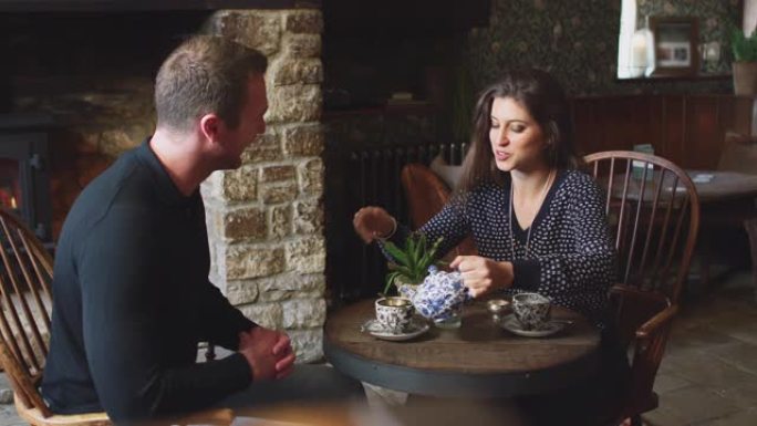 夫妇坐在餐桌旁，在传统的英国度假酒店里倒茶-慢动作拍摄