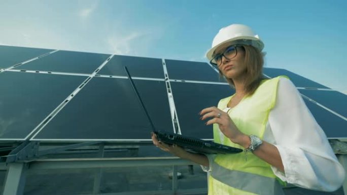 女建造师正带着电脑沿着太阳能电池板行走