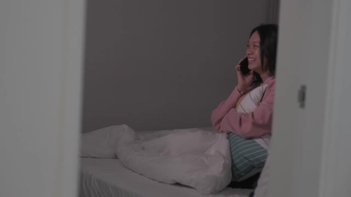 一名亚裔华裔女性晚上在卧室的床上通过电话交谈，情绪积极