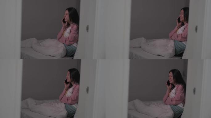 一名亚裔华裔女性晚上在卧室的床上通过电话交谈，情绪积极