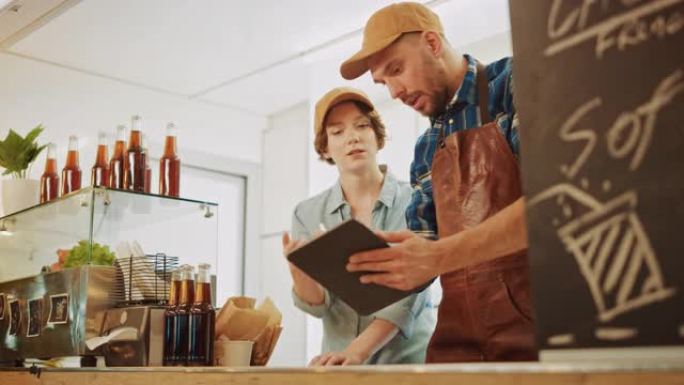 成功的食品卡车男女员工戴着棕色帽子正在使用平板电脑。他们讨论他们的利润和未来的商业计划。出售街头食品
