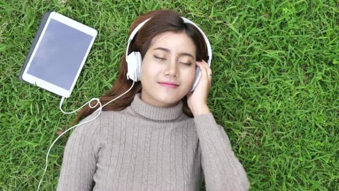 年轻女子少年躺在草地上的耳机上享受最喜欢的音乐