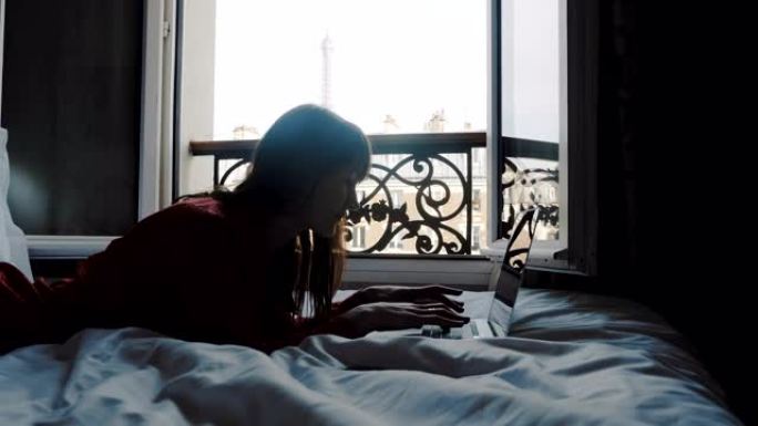 快乐微笑的高加索作家躺在法国阳台床上的笔记本电脑上打字，在旅行慢动作中寻找灵感。