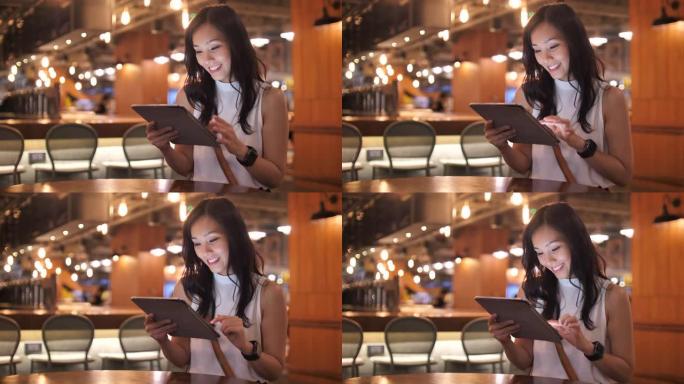 穿着休闲服装的年轻亚洲女性在咖啡馆使用数字平板触摸屏电脑