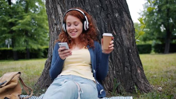 微笑的女孩在公园里用智能手机在耳机里听音乐