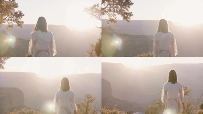 穿着白色连衣裙的年轻幸福女人的电影背光镜头，在日落时欣赏令人惊叹的大峡谷全景。