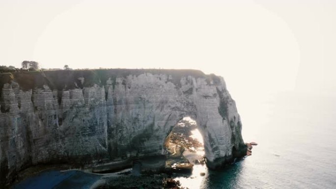 无人机正在著名的白诺曼底悬崖上的史诗般的自然岩石拱门中逃离年轻快乐的旅游新婚夫妇