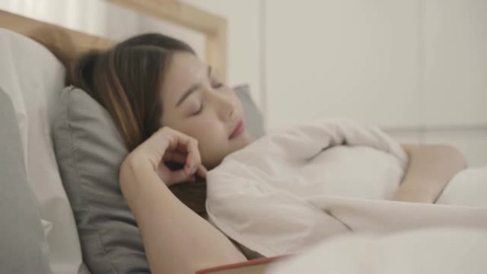 美丽的年轻亚洲女子躺在床上看书，女性睡觉后在家卧室放松。生活方式女性使用在家放松时间的概念。