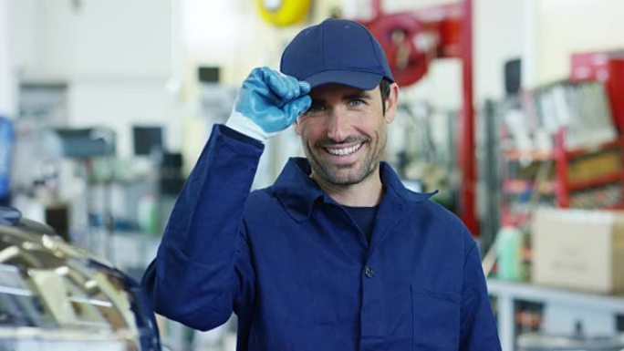 在车库里，使用平板电脑的机械师使机油和发动机检查对汽车微笑。