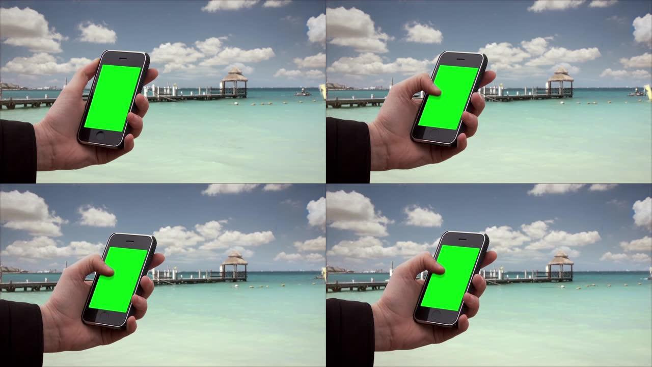 在热带海滩上，男性双手握着带有绿色屏幕的旧智能手机。