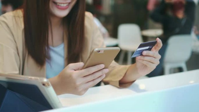 4k镜头亚洲妇女使用信用卡和手机在线购物的场景在百货公司的共同工作空间无现金，科技钱包和在线支付概念