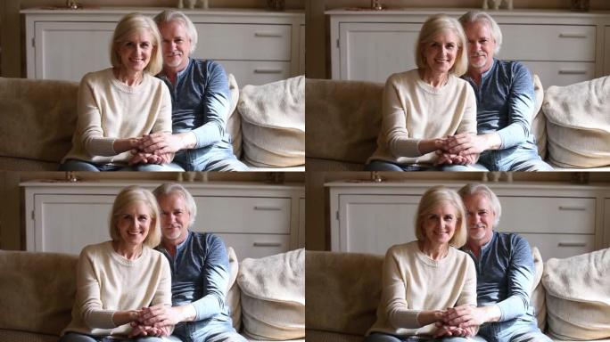 老年夫妇坐在沙发上手牵手看着相机
