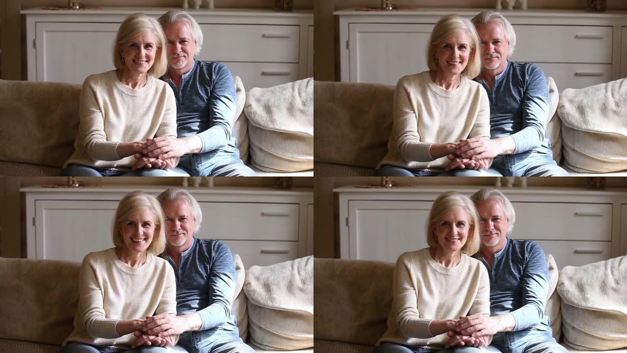 老年夫妇坐在沙发上手牵手看着相机