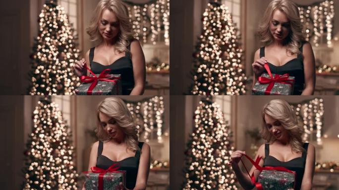 一个穿着晚礼服的美丽金发女郎在圣诞树的背景上看着她的礼物。