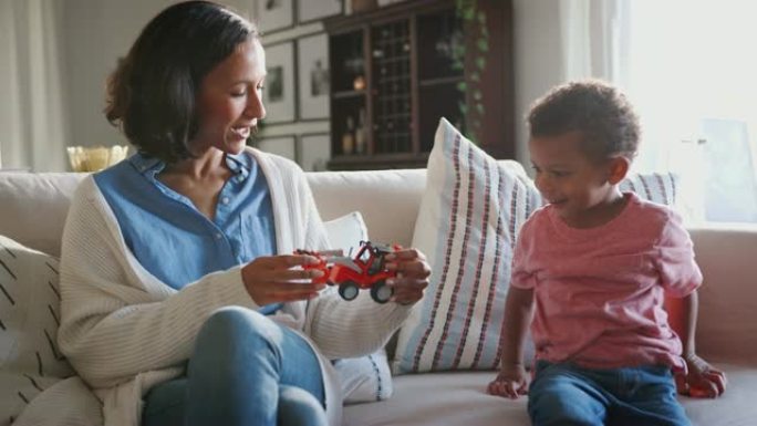 年轻的混血母亲坐在沙发上与三岁的儿子在家里玩耍，特写