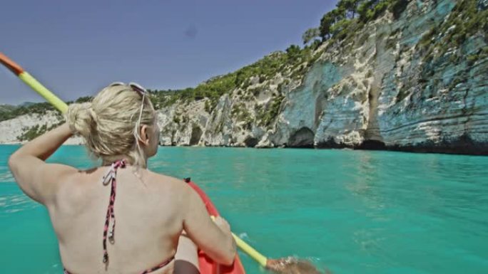 年轻女子女士在意大利普利亚悬崖下阳光明媚的绿松石海上划独木舟