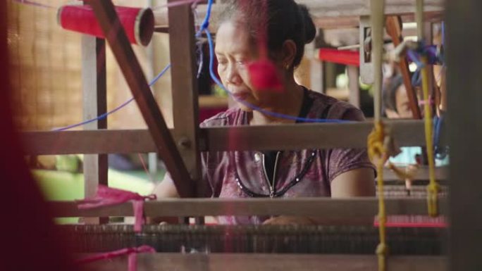一位泰国老年妇女根据古老的传统编织衣服并手工编织。