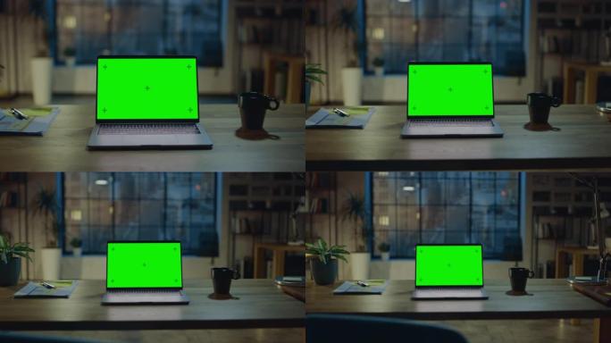 模拟绿屏笔记本电脑站在现代创意办公室的桌子上。背景中温暖的晚间照明和开放空间工作室与城市窗口视图。缩