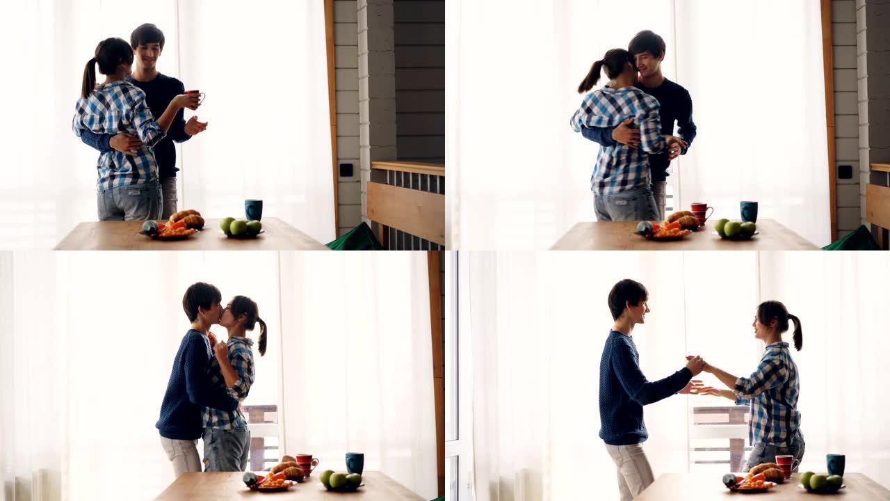 可爱的女孩和男孩在厨房喝茶，然后在早餐后跳舞和亲吻，表达感情并享受休闲时光。爱情和家庭概念。
