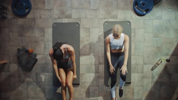 两名专业的女性健美运动员躺在硬核健身房的瑜伽垫上做仰卧起坐运动。肌肉发达，运动优美的女孩锻炼和庆祝的