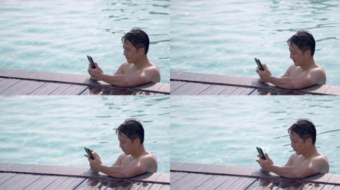 亚洲男子度假时在游泳池里使用电话