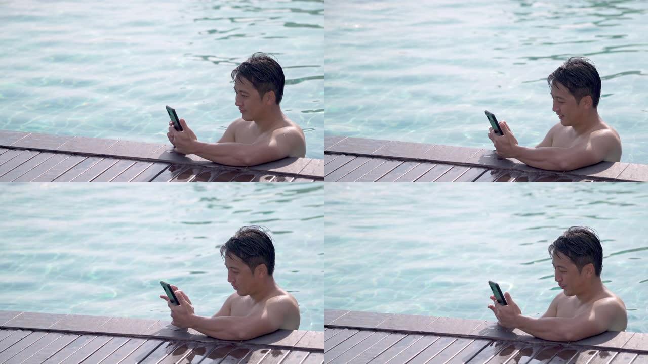 亚洲男子度假时在游泳池里使用电话