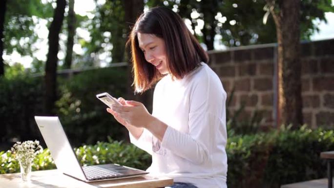 女性工作与她的笔记本电脑，使用智能手机和微笑在室外花园在家