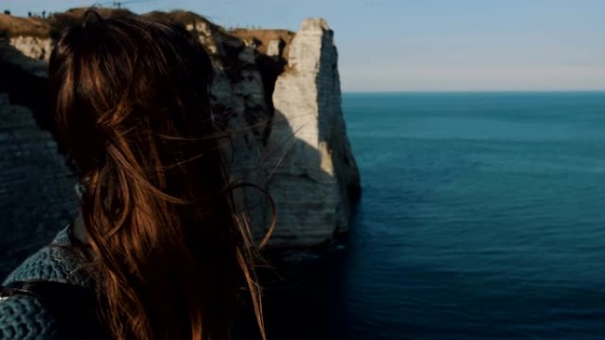 后视图年轻的黑发旅行者女人在埃特雷塔看着史诗般的自然风景，头发在风中吹慢动作。