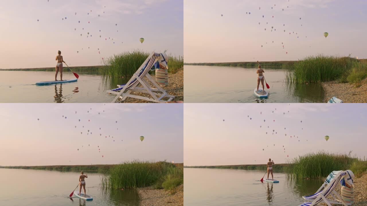 SLO MO女人划桨，而热气球在湖上飞行