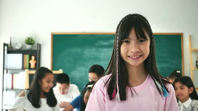 小女孩的肖像在她的教室里看着相机，背景是她的朋友。