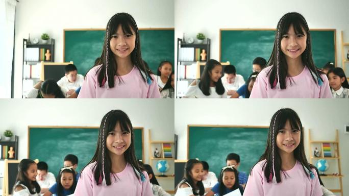 小女孩的肖像在她的教室里看着相机，背景是她的朋友。