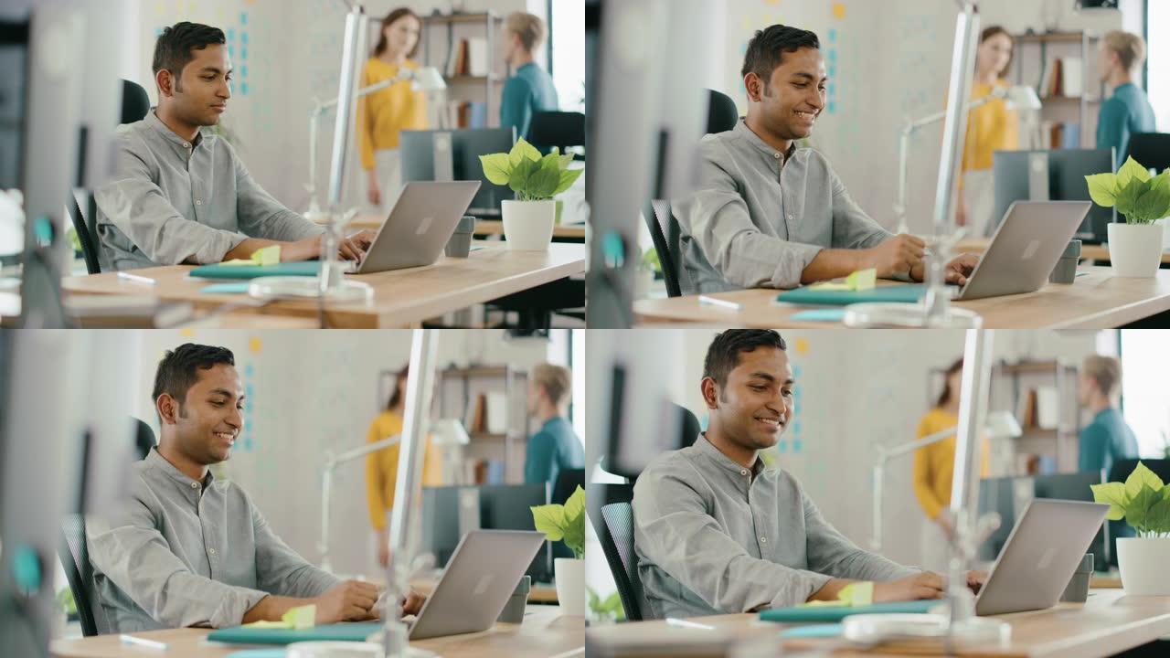 坐在办公桌前的聪明英俊的印度上班族在笔记本电脑上工作。成功的人会做 “是” 的手势并庆祝。在现代办公